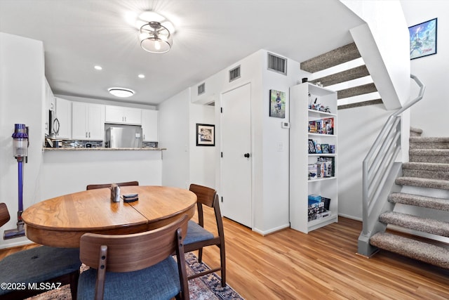 dining area with light wood finished floors, stairway, and visible vents