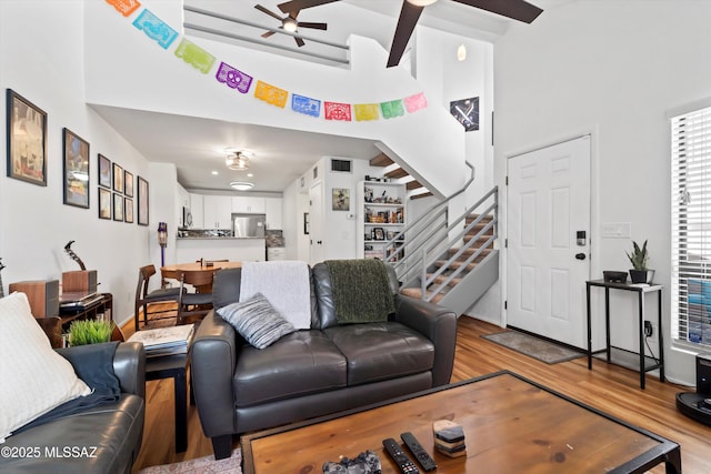 living area with visible vents, wood finished floors, ceiling fan, and stairs