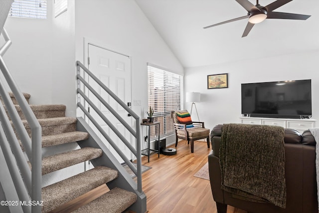 living area with high vaulted ceiling, stairway, light wood-style floors, and a ceiling fan