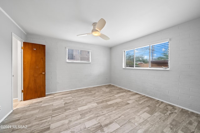 unfurnished room with wood finished floors, a ceiling fan, and brick wall