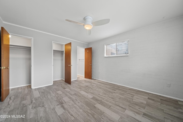 unfurnished bedroom with brick wall, baseboards, multiple closets, wood finished floors, and a ceiling fan