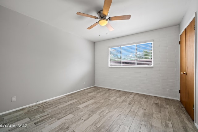 spare room featuring wood finished floors, baseboards, brick wall, and ceiling fan