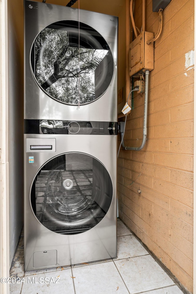 laundry room with laundry area, stacked washer / dryer, and brick wall