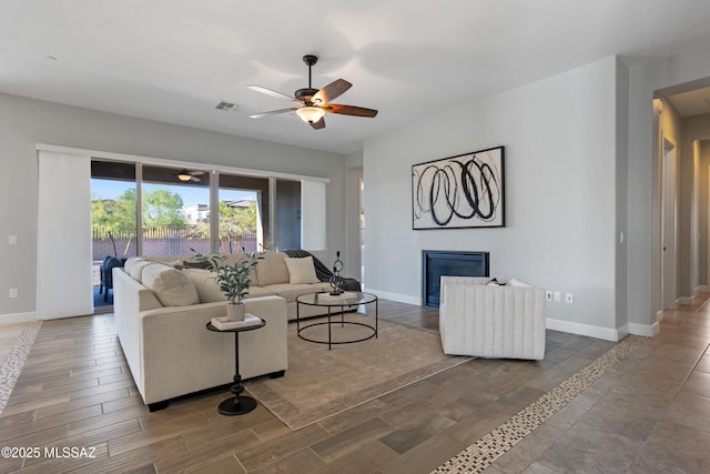 living area featuring visible vents, wood finished floors, a glass covered fireplace, and a ceiling fan