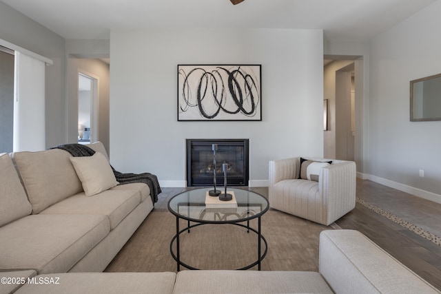 living room featuring a glass covered fireplace, baseboards, and wood finished floors