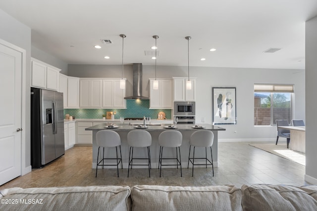 kitchen with visible vents, a breakfast bar, backsplash, appliances with stainless steel finishes, and wall chimney exhaust hood