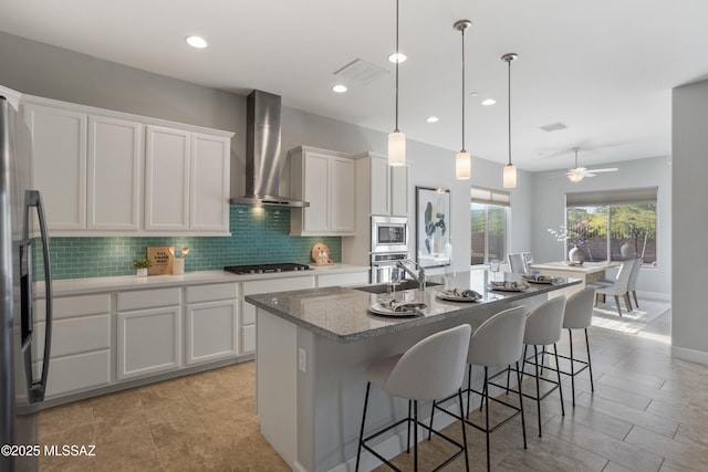 kitchen with visible vents, tasteful backsplash, appliances with stainless steel finishes, white cabinets, and wall chimney range hood