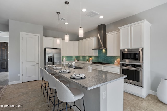 kitchen featuring visible vents, backsplash, stainless steel appliances, wall chimney exhaust hood, and a sink