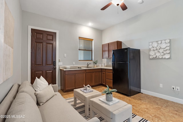 kitchen with baseboards, freestanding refrigerator, ceiling fan, a sink, and light countertops