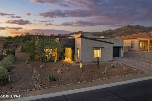 view of front facade with stucco siding, decorative driveway, an attached garage, and a mountain view