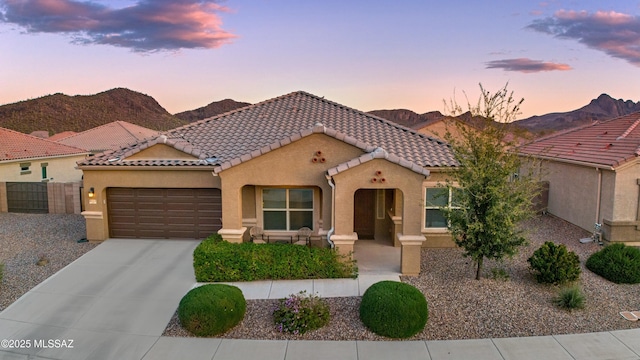 mediterranean / spanish-style home featuring driveway, an attached garage, stucco siding, a tiled roof, and a mountain view