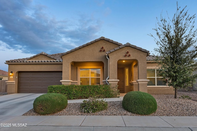 mediterranean / spanish home featuring stucco siding, concrete driveway, a tile roof, and a garage