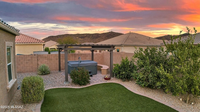 yard at dusk featuring a hot tub and a fenced backyard