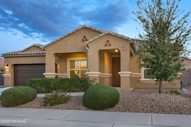 mediterranean / spanish-style house featuring a tile roof, an attached garage, and stucco siding