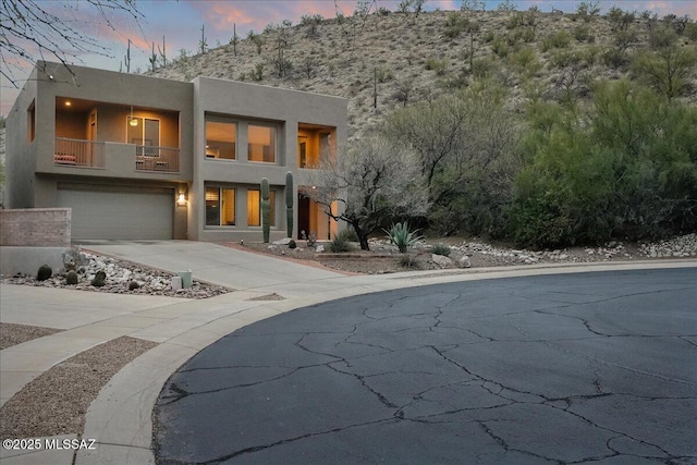 view of front facade with a balcony, an attached garage, driveway, and stucco siding