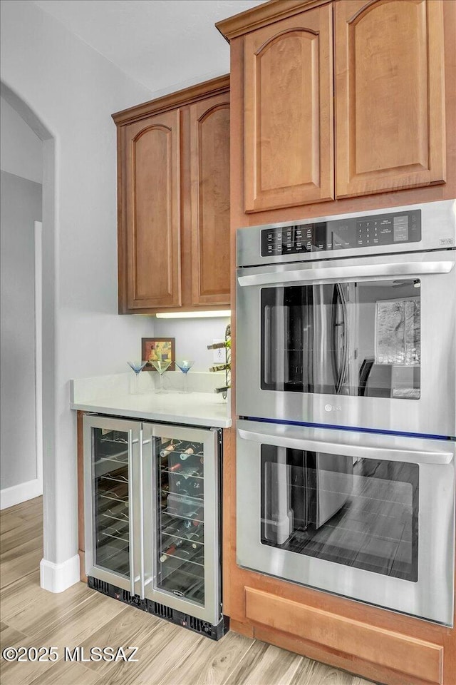 kitchen with beverage cooler, baseboards, stainless steel double oven, light countertops, and light wood-style floors