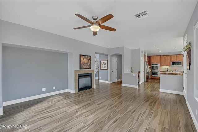 unfurnished living room with light wood-style floors, ceiling fan, arched walkways, visible vents, and baseboards
