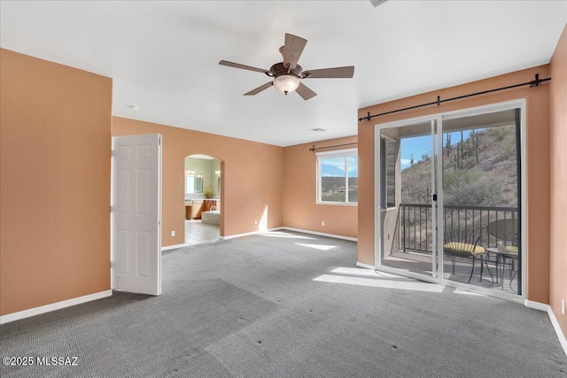 carpeted spare room featuring arched walkways, baseboards, and a ceiling fan