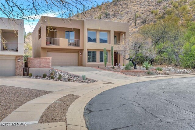 pueblo-style home featuring concrete driveway, a balcony, stucco siding, and an attached garage