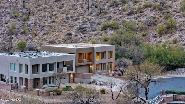 rear view of property with a balcony, stucco siding, driveway, and a garage