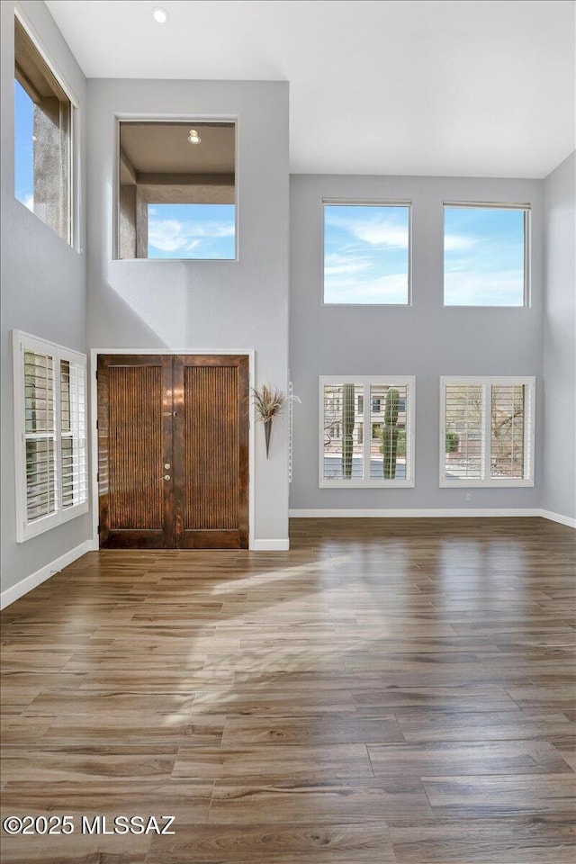 unfurnished living room featuring baseboards, recessed lighting, a high ceiling, and wood finished floors