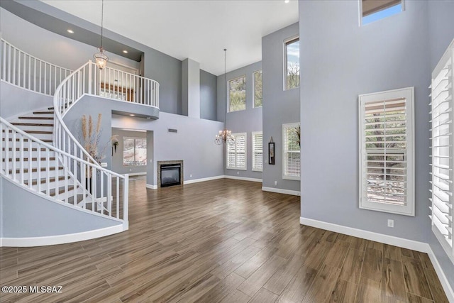 unfurnished living room with baseboards, wood finished floors, a towering ceiling, and stairs