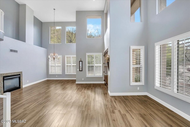 unfurnished living room featuring an inviting chandelier, a towering ceiling, a glass covered fireplace, visible vents, and wood finished floors