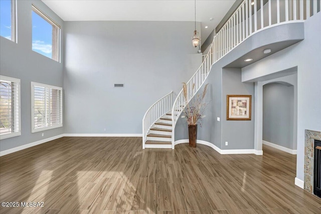 unfurnished living room with a towering ceiling, baseboards, stairway, arched walkways, and wood finished floors