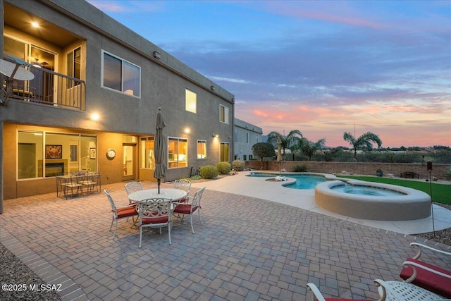 pool at dusk featuring a pool with connected hot tub, outdoor dining area, and a patio