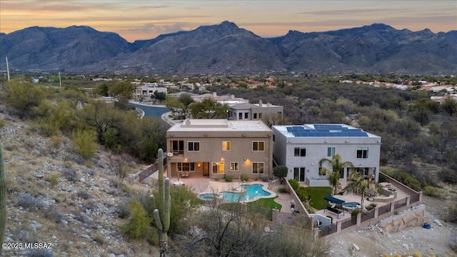 back of house at dusk with a patio, a fenced backyard, a mountain view, and roof mounted solar panels