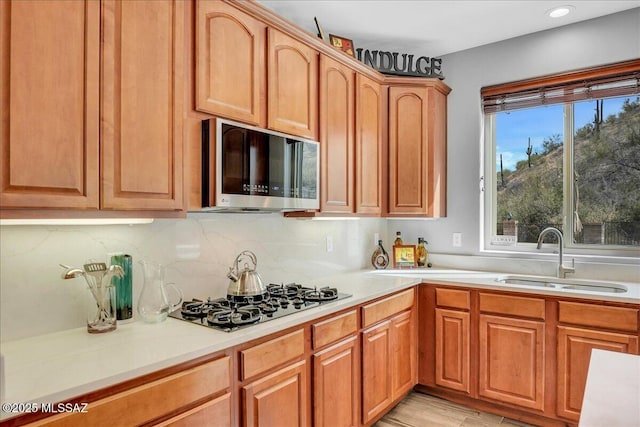 kitchen featuring black gas stovetop, a sink, stainless steel microwave, light countertops, and decorative backsplash