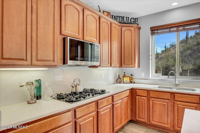 kitchen featuring tasteful backsplash, stainless steel microwave, a sink, light countertops, and black gas stovetop
