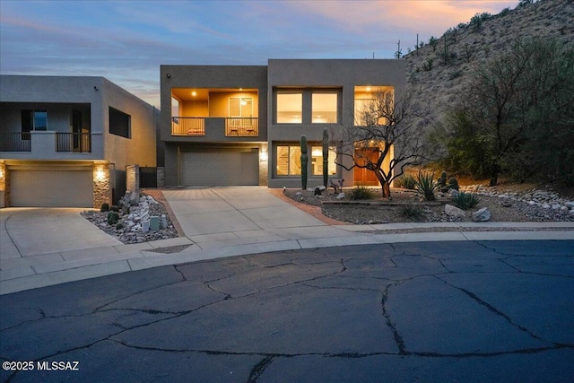 contemporary house with stucco siding, driveway, stone siding, an attached garage, and a balcony