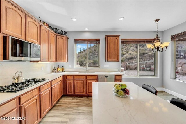 kitchen featuring stainless steel microwave, a notable chandelier, black gas stovetop, light wood-style floors, and a sink