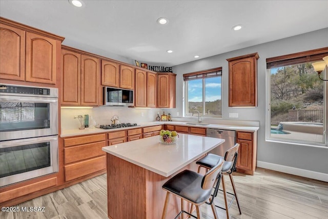 kitchen with a sink, light countertops, a kitchen breakfast bar, recessed lighting, and stainless steel appliances