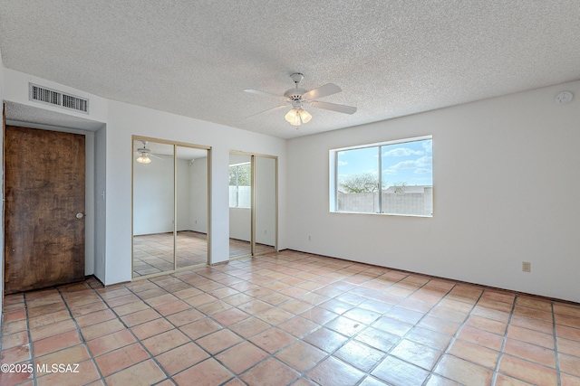 unfurnished bedroom with visible vents, two closets, a ceiling fan, a textured ceiling, and light tile patterned floors