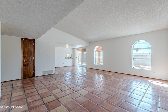 empty room with a textured ceiling, tile patterned floors, visible vents, and vaulted ceiling