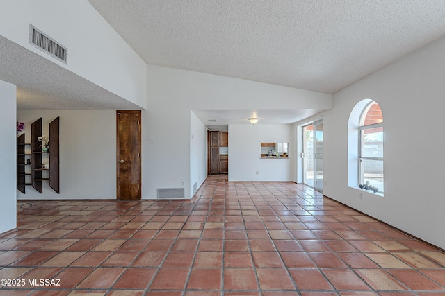 tiled empty room with visible vents, a textured ceiling, and vaulted ceiling