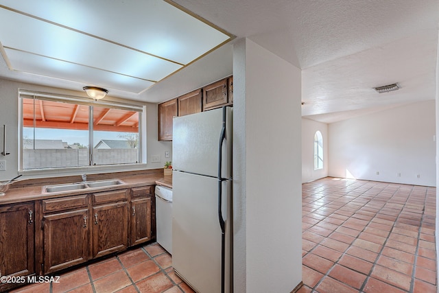 kitchen with visible vents, light tile patterned floors, white appliances, a textured ceiling, and a sink