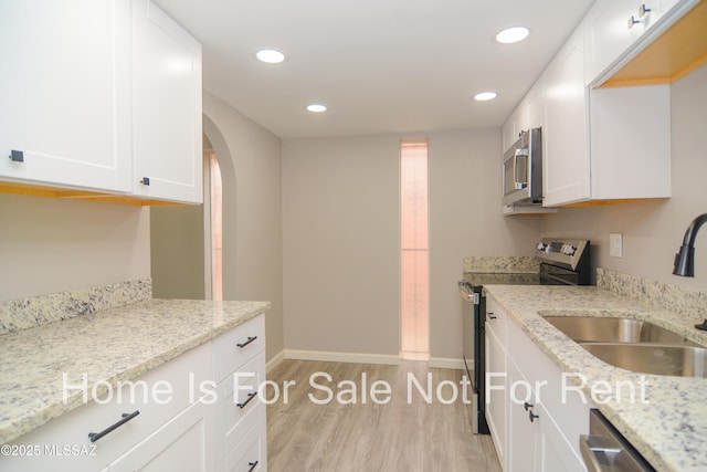 kitchen featuring arched walkways, a sink, stainless steel appliances, white cabinets, and light wood-style floors