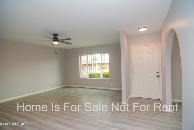 foyer entrance with wood finished floors, baseboards, arched walkways, and ceiling fan