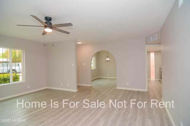 spare room featuring arched walkways, visible vents, a ceiling fan, and wood finished floors