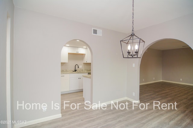 spare room featuring visible vents, a sink, arched walkways, light wood finished floors, and baseboards