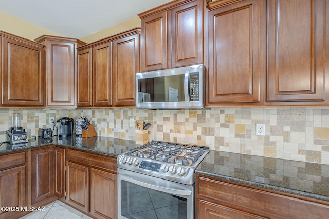 kitchen with brown cabinetry, dark stone counters, tasteful backsplash, and stainless steel appliances