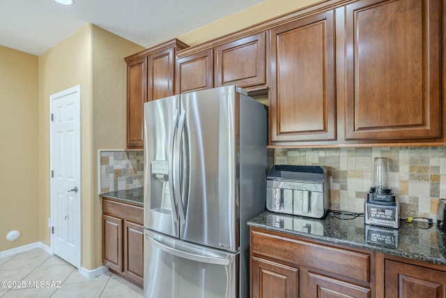 kitchen with stainless steel refrigerator with ice dispenser, brown cabinetry, decorative backsplash, and dark stone countertops