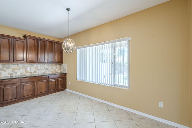kitchen featuring a notable chandelier, dark stone counters, decorative light fixtures, baseboards, and decorative backsplash