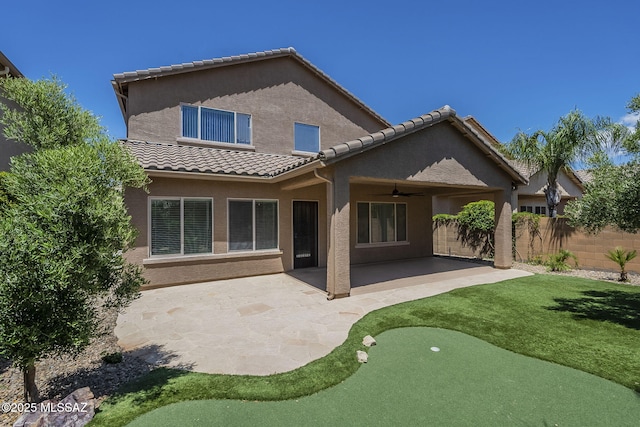 rear view of property featuring fence, ceiling fan, stucco siding, a patio, and a tiled roof