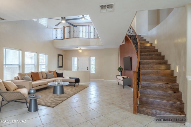 living room featuring ceiling fan, visible vents, light tile patterned floors, a high ceiling, and stairs