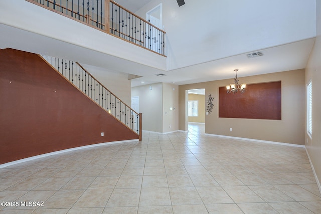unfurnished living room with tile patterned floors, a chandelier, baseboards, a towering ceiling, and visible vents