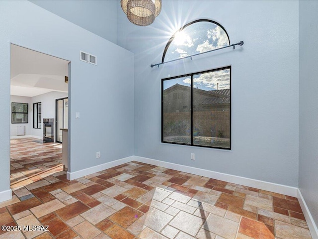 empty room featuring stone tile flooring, visible vents, a high ceiling, and baseboards